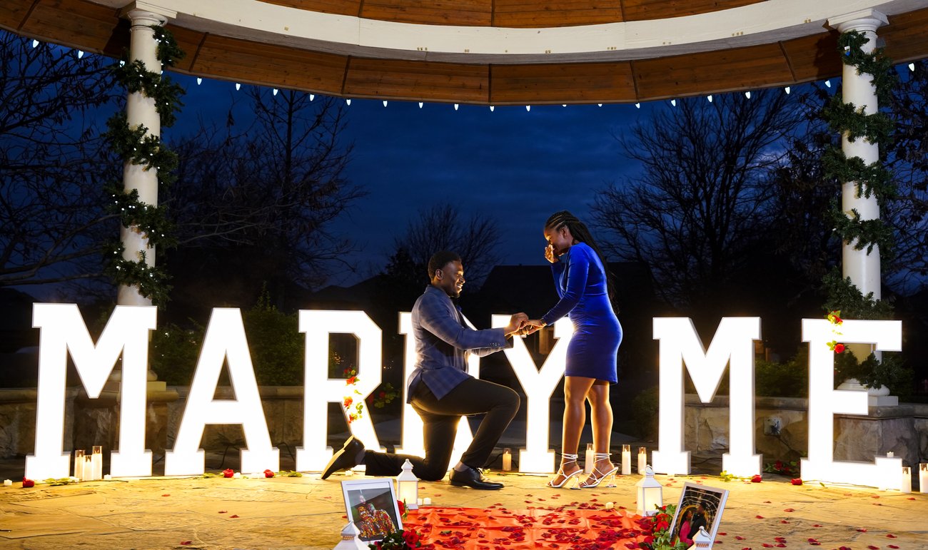 Marriage proposal under a lit Marry Me sign